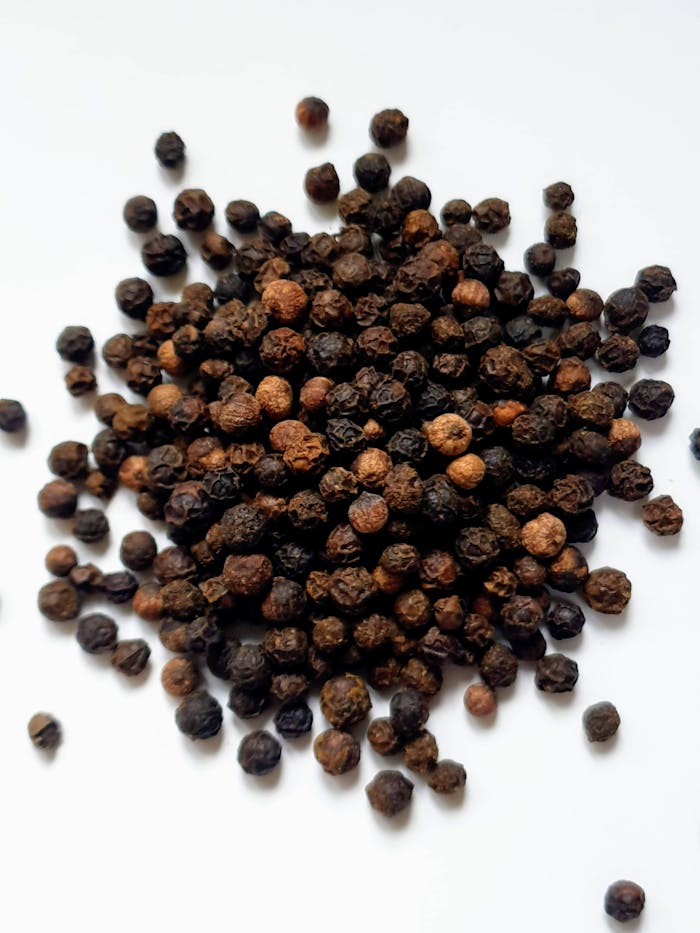 A close-up shot of black peppercorns scattered on a white surface.